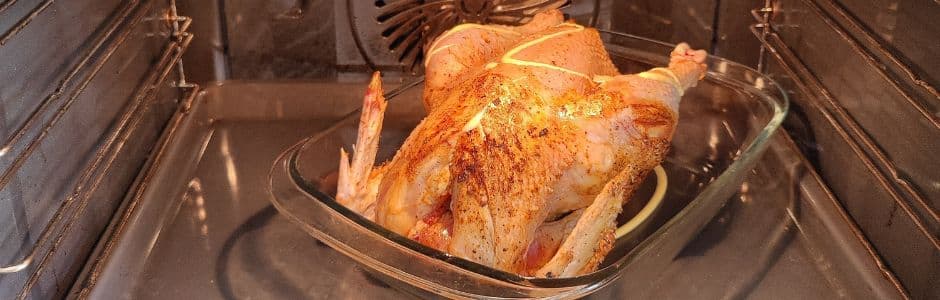 Een beeld van een gekruide kip in een oven, klaar om te worden gebakken. Het vel van de kip is bedekt met kruiden en smaakmakers zoals ui, look en citroen, en er is boter of olie toegevoegd aan de binnenkant van de kip.